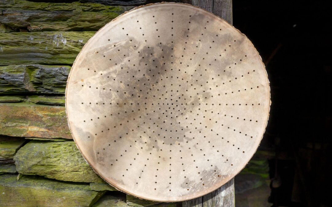 Criva tradicional gallega hecha de piel perforada, utilizada para cribar o tamizar el grano, apoyada sobre una pared de piedra.